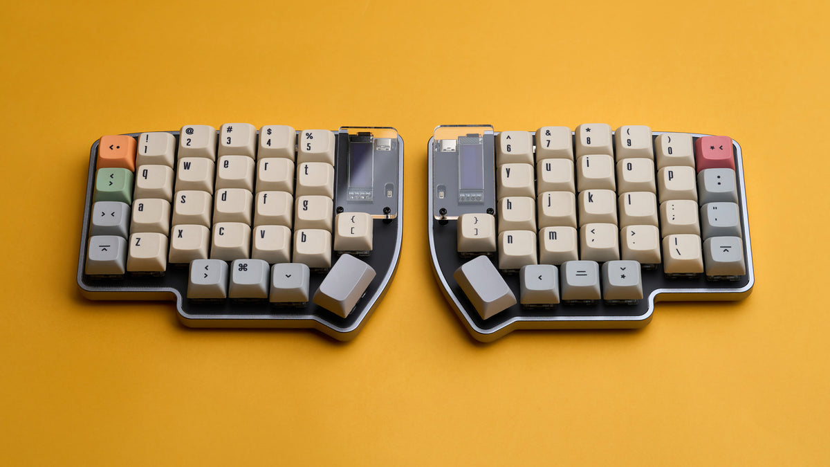 Wide shot of Lily Pad keyboard with beige and gray keycaps, orange Esc key, and OLED displays on yellow background.