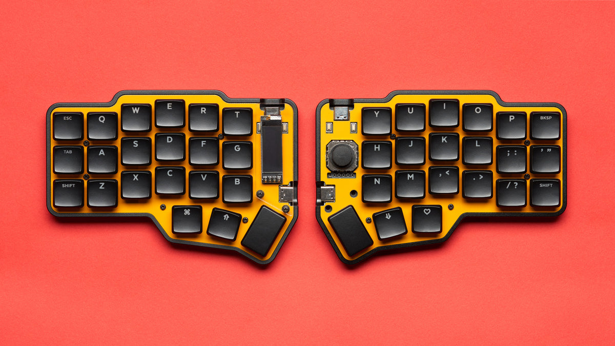 Fully assembled Unicorne LP keyboard in black with yellow plates, with Choc keycaps and OLEDs and joysticks, shown from top-down on red background